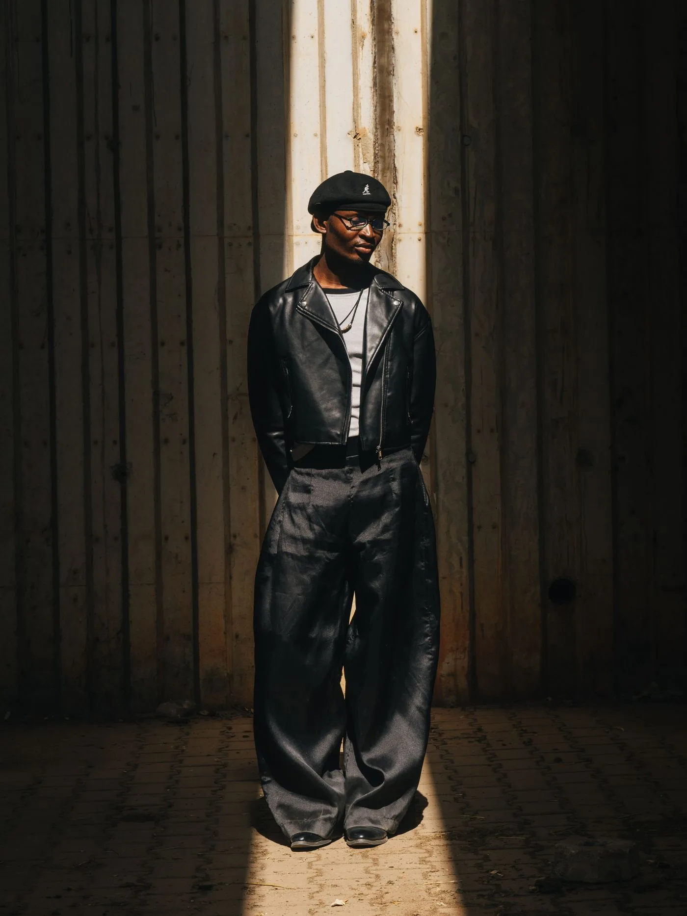 A person in a dark jacket and wide dark trousers standing in sunlight