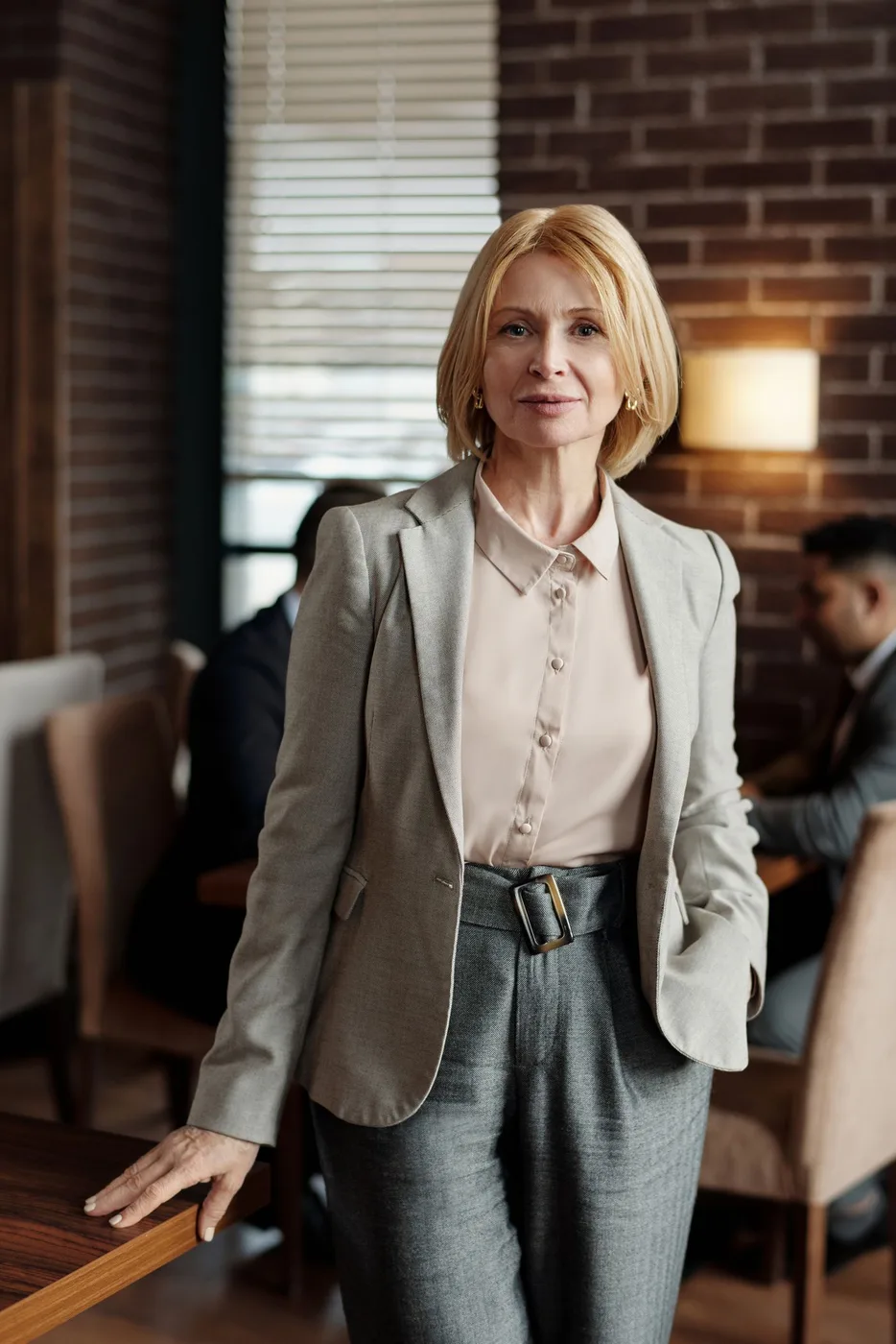 A woman in a light blazer and blouse with gray tailored trousers indoors