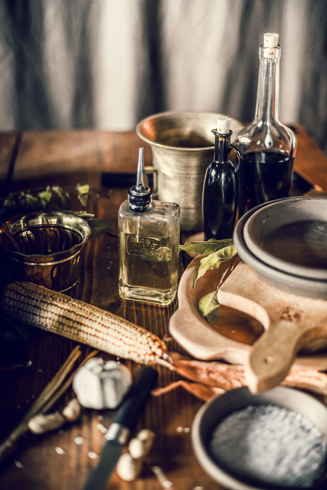 Metal kitchen utensils, bottles and crockery arranged on a wooden table