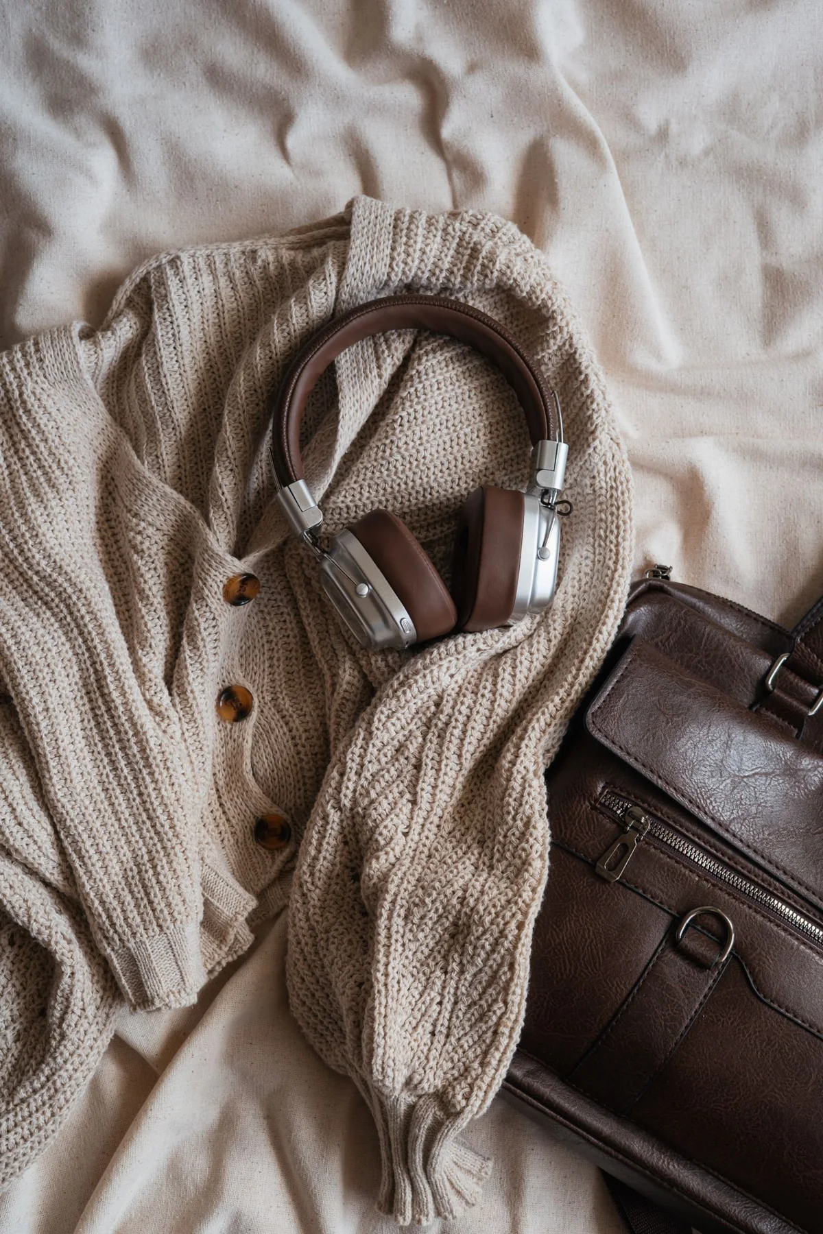 Brown knitwear arranged with headphones and a leather-looking bag on a surface.