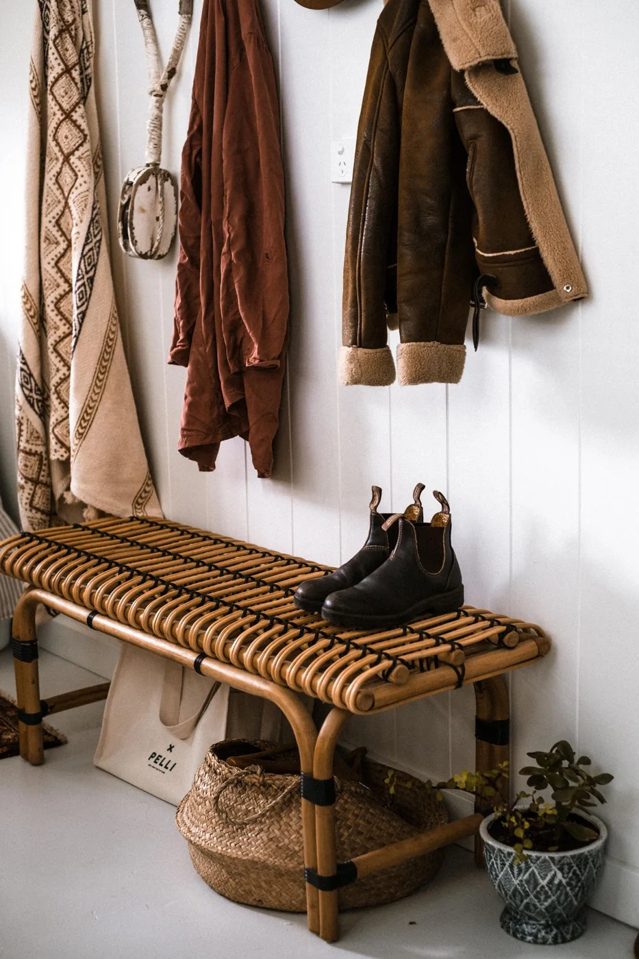 An entryway with hanging coats and a woven bench