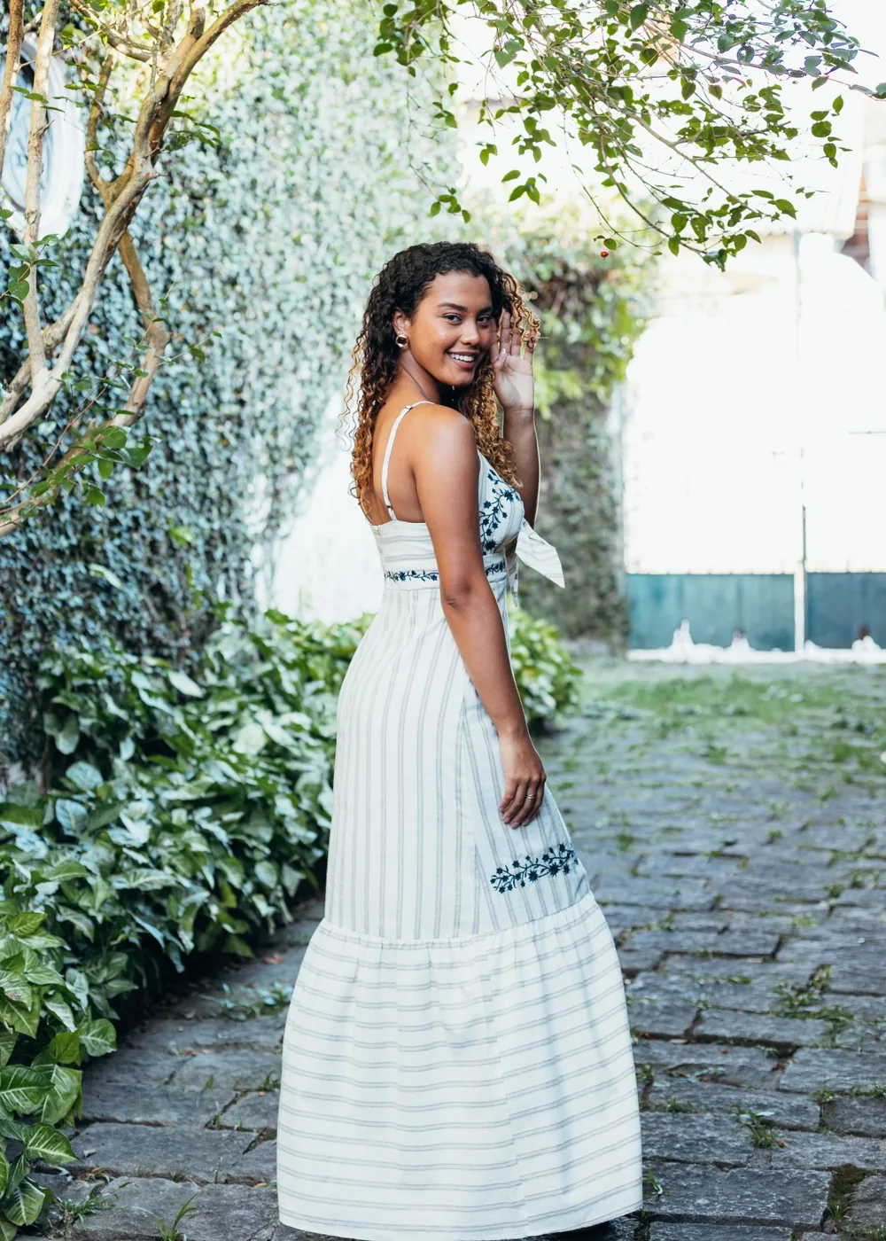 A woman wearing a pale dress on a sunlit garden path