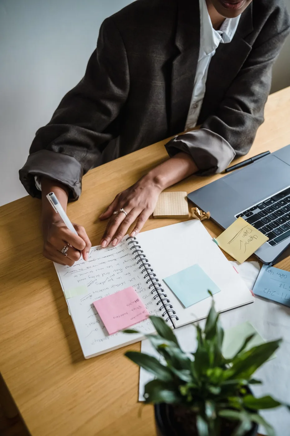Hands writing in a notebook beside a computer and stationery