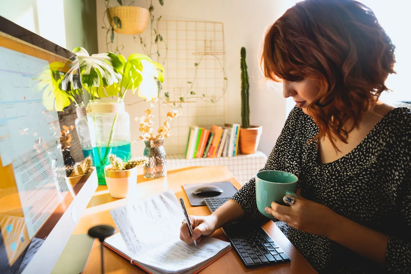 A woman holding a mug while writing in a notebook at a table