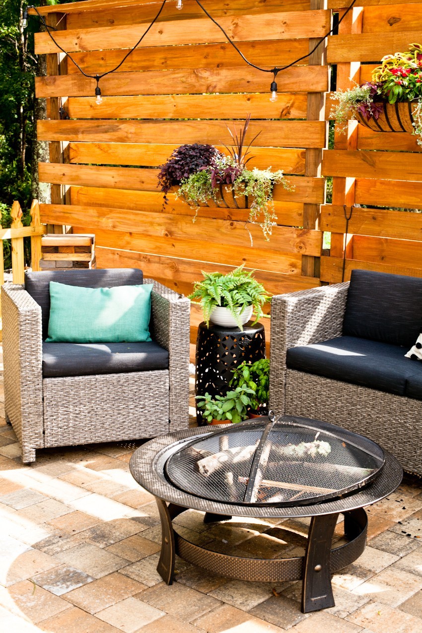Makeover your backyard space and get ready for grilling season with a slat privacy fence DIY! | Grilling Season by popular Florida lifestyle blog, Fresh Mommy Blog: image of a vertical platen wall, wicker chairs with dark grey cushions and potted plants.
