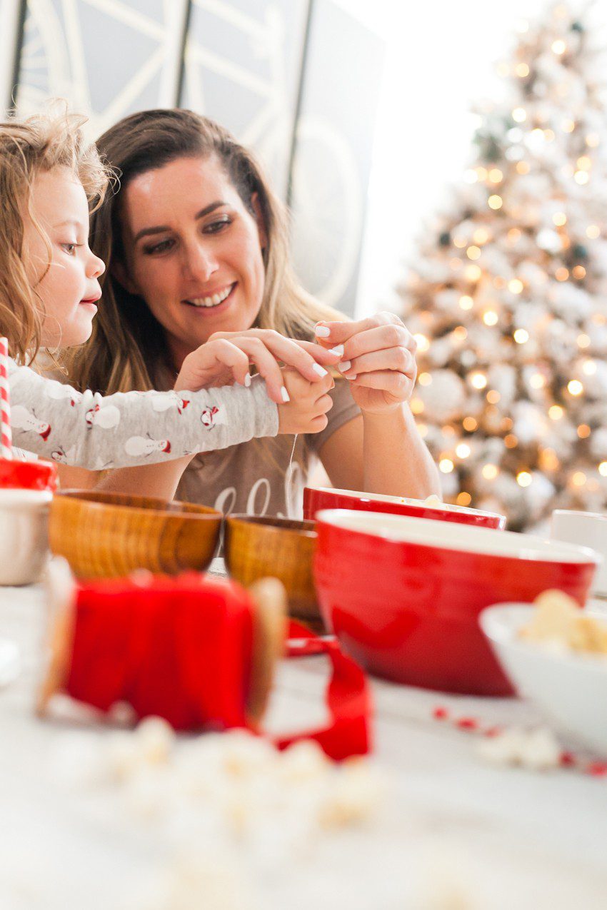 How to Host your Own Festive Tree Trimming Party from top Florida lifestyle blogger Tabitha Blue of Fresh Mommy Blog: image of mom and daughter making Christmas tree decorations with popcorn