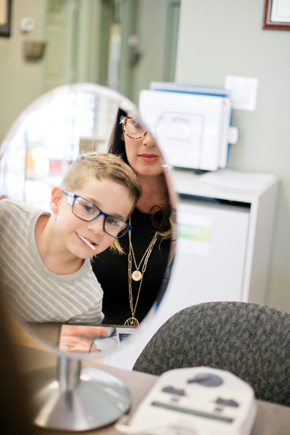 Back to School Eye Exam: How to Prepare your Child for a Successful Academic Year | Back to School Eye Exam: How to Prepare your Child for a Successful Academic Year by popular Florida lifestyle blog, Fresh Mommy Blog: image of a mom and her son looking at themselves in a mirror and trying on a pair of glasses.