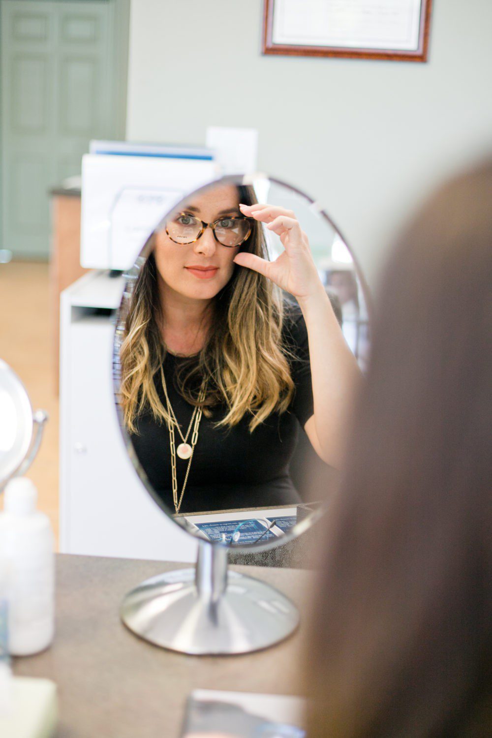 Back to School Eye Exam: How to Prepare your Child for a Successful Academic Year | Back to School Eye Exam: How to Prepare your Child for a Successful Academic Year by popular Florida lifestyle blog, Fresh Mommy Blog: image of a woman looking at herself in a mirror and trying on a pair of glasses.
