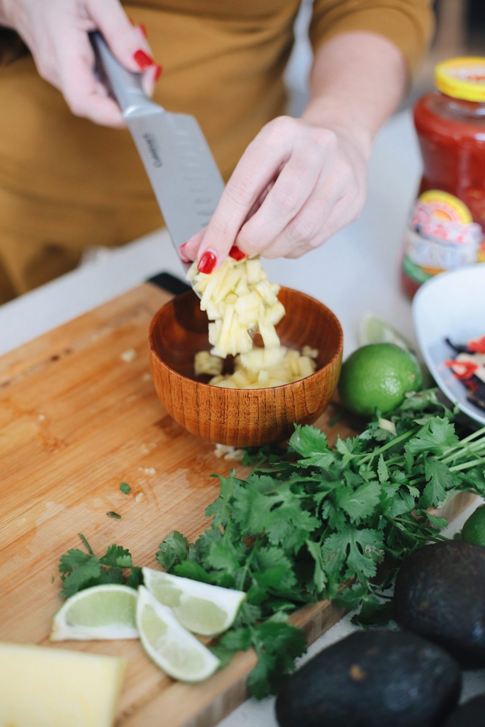Avocado Keto Taco Bowls recipe featured by top Florida lifestyle blog, Fresh Mommy Blog: Chopped pineapple for the best taco bowl, a delicious twist for taco night | Keto Taco Bowls by popular Florida lifestyle blog, Fresh Mommy Blog: image of a woman putting pineapple chunks in a bowl.