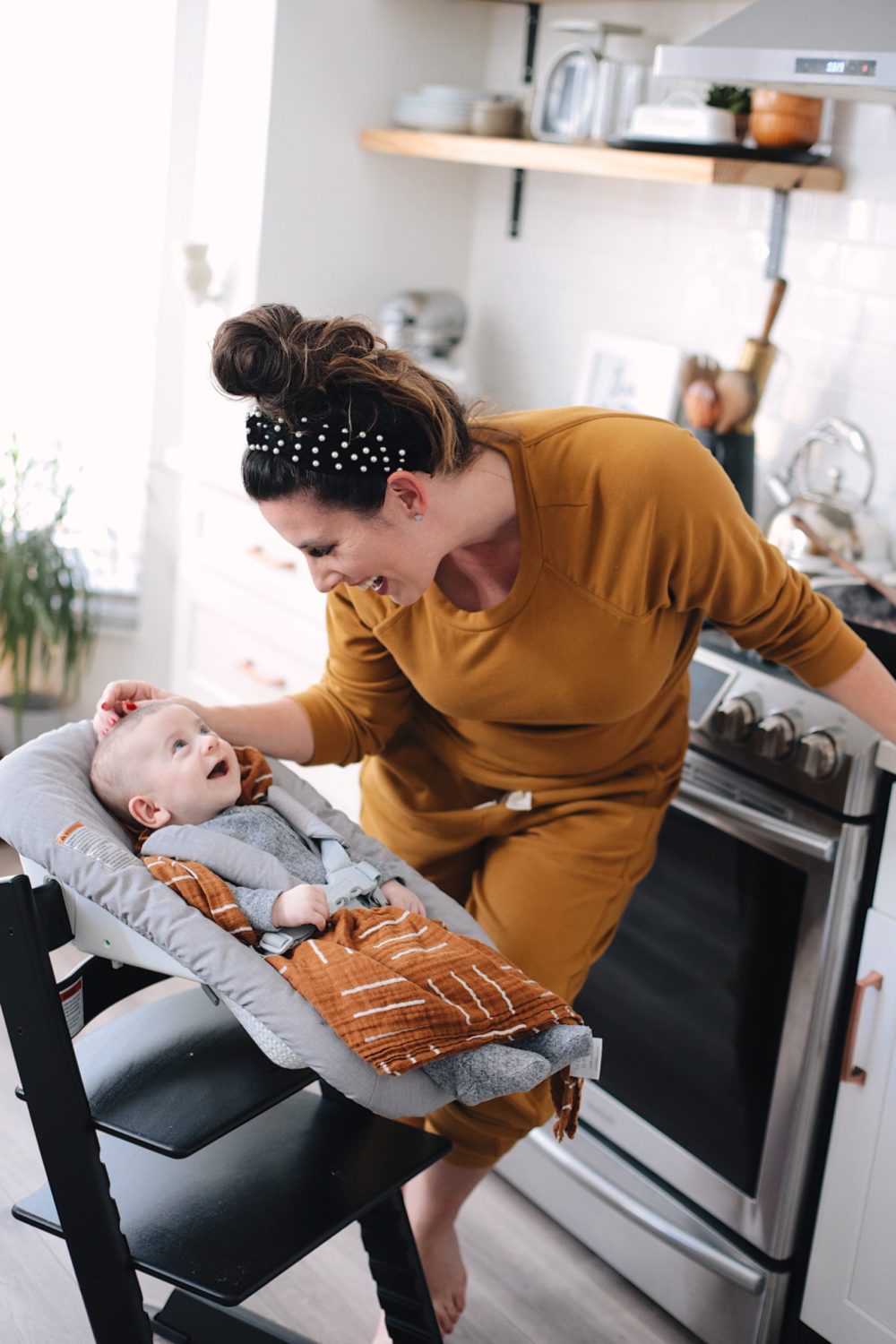 Avocado Keto Taco Bowls recipe featured by top Florida lifestyle blog, Fresh Mommy Blog: Mama cooking in the kitchen with her baby - stokke tripp chair high chair for newborn | Keto Taco Bowls by popular Florida lifestyle blog, Fresh Mommy Blog: image of a mom smiling at her baby in a stokke chair and rubbing her baby's head.