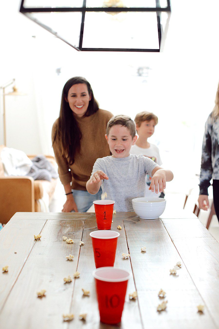 10 Popcorn Games for a Great Family Fun Night | Family Fun Night by popular Florida lifestyle blog, Fresh Mommy Blog: image of a mom and her kids tossing popcorn into red plastic cups. 