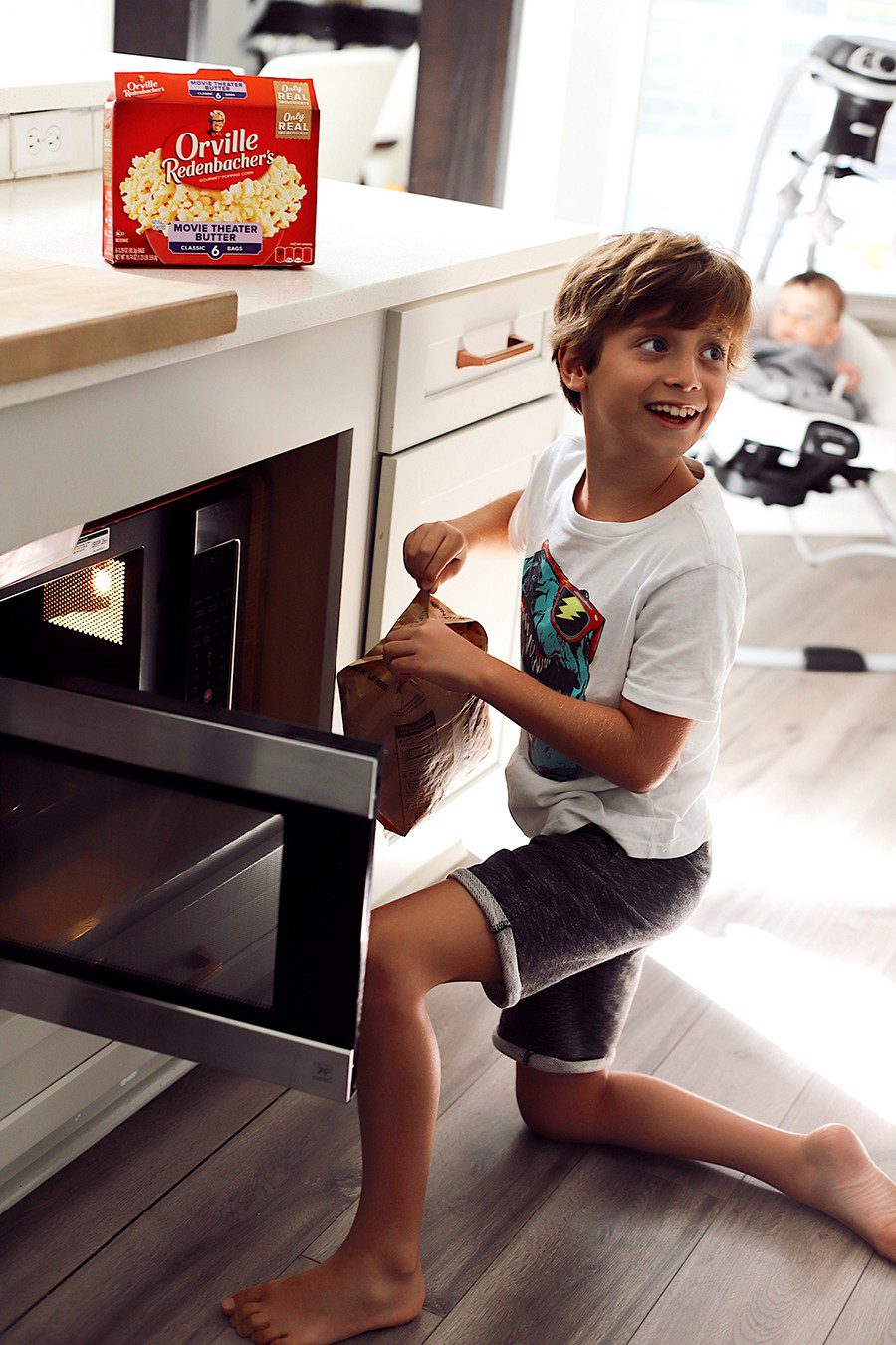 10 Popcorn Games for a Great Family Fun Night | Family Fun Night by popular Florida lifestyle blog, Fresh Mommy Blog: image of a boy holding a bag of Orville Redenbacher's microwave popcorn next to a open microwave. 