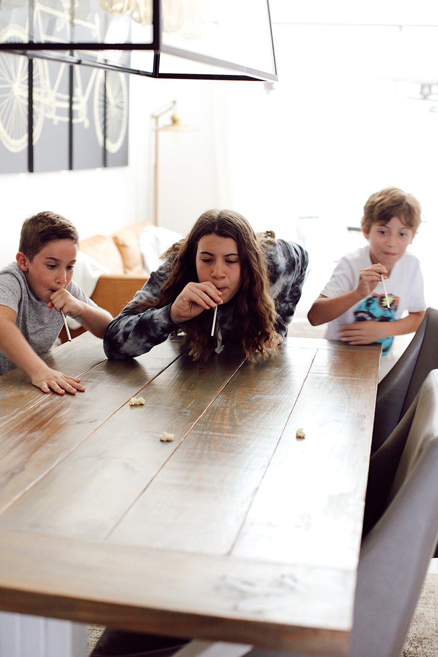 Popcorn race and more fun popcorn games for family game night! | Family Fun Night by popular Florida lifestyle blog, Fresh Mommy Blog: image of some kids blowing a piece of popcorn across a table with some straws. 