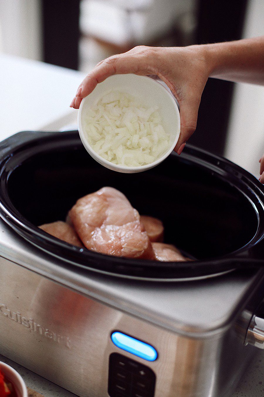 Chicken Tacos by popular Florida lifestyle blog, Fresh Mommy Blog: image of Tabitha Blue pouring chopped onions into a crockpot. 